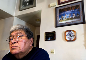 Muralist Alex Seowtewa sits in front of a photograph of the mural on the south wall of the Nuestra Senora de Guadalupe Mission at his home in Zuni on Jan. 13. Seowtewa has spent several decades painting the new crumbling mural. Independent file photo. 